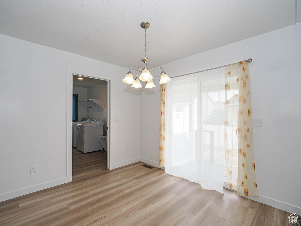Unfurnished room featuring independent washer and dryer, a chandelier, light wood-type flooring, and baseboards