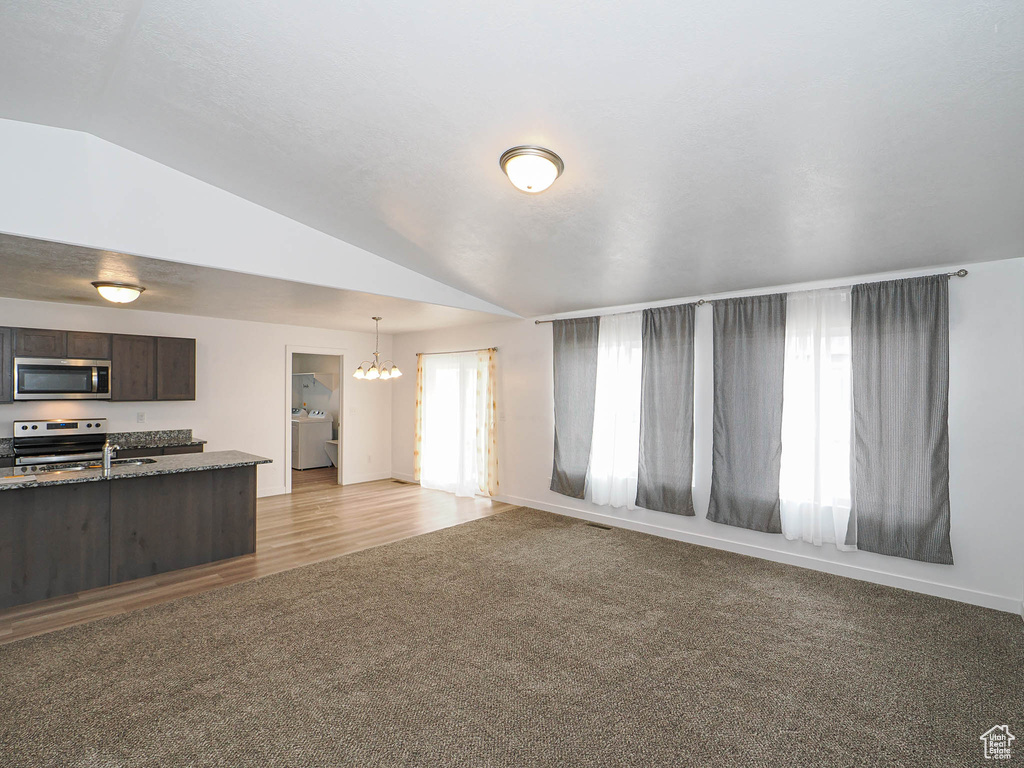 Kitchen featuring stainless steel appliances, washer / dryer, lofted ceiling, a chandelier, and dark brown cabinets
