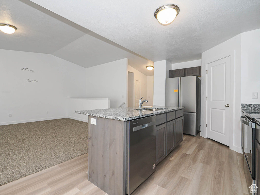 Kitchen featuring stainless steel appliances, light stone counters, light wood finished floors, a center island with sink, and a sink