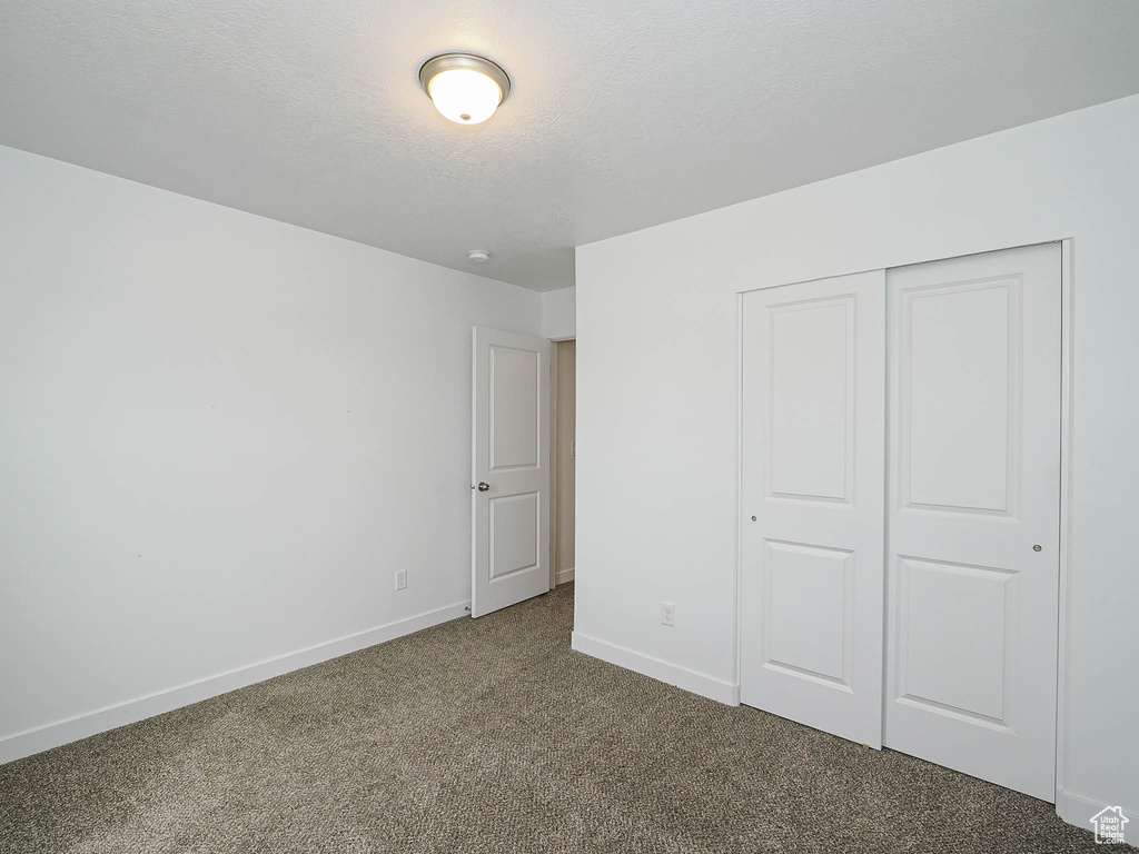 Unfurnished bedroom featuring carpet flooring, a textured ceiling, baseboards, and a closet