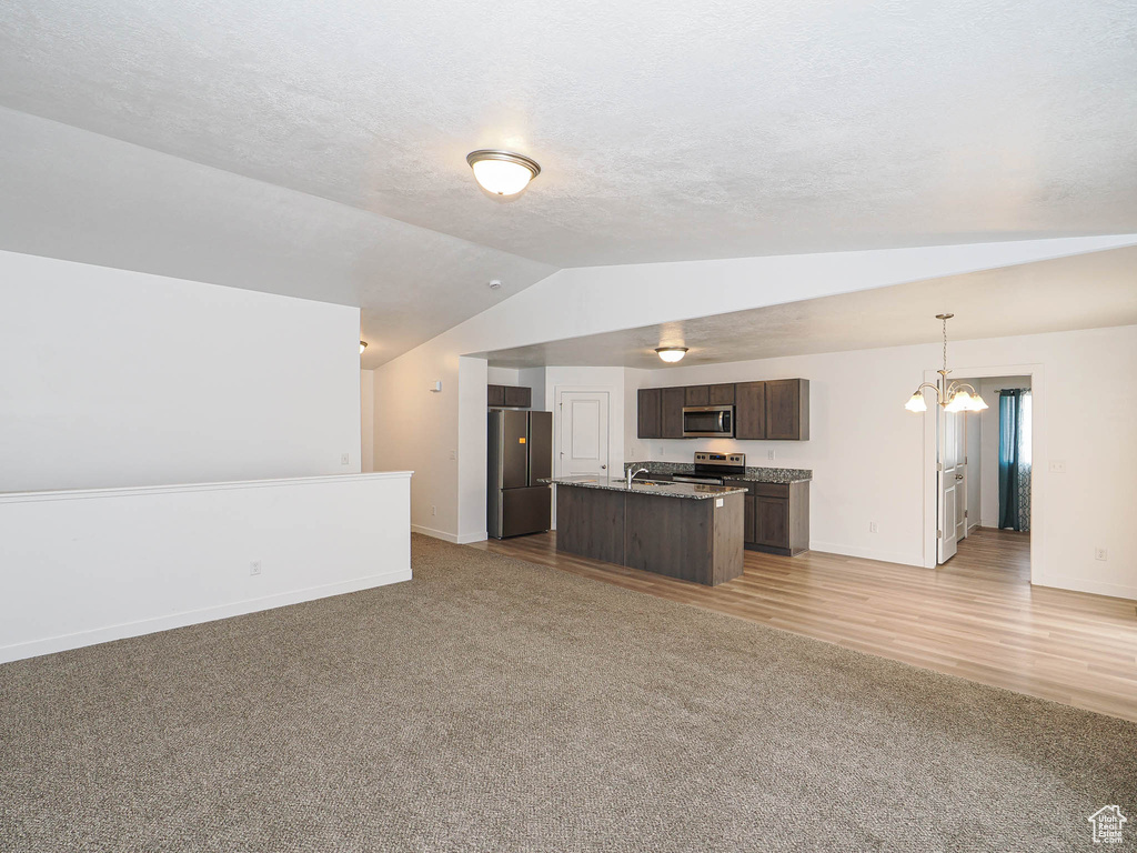 Kitchen with open floor plan, appliances with stainless steel finishes, lofted ceiling, light carpet, and dark brown cabinets