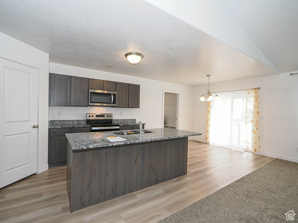Kitchen with stainless steel appliances, a sink, a chandelier, dark stone counters, and light wood finished floors