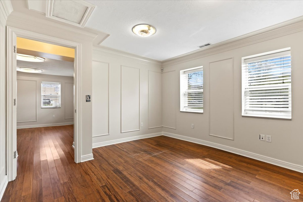Spare room with dark wood-style flooring, crown molding, baseboards, attic access, and a decorative wall