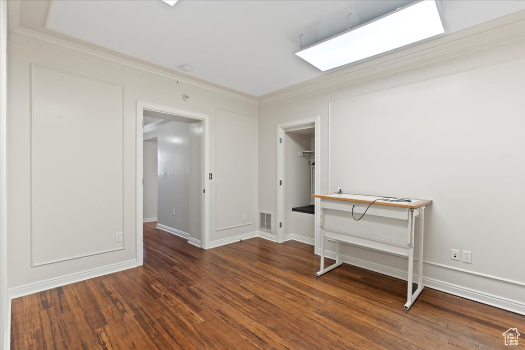 Unfurnished room featuring a skylight, crown molding, wood finished floors, and baseboards