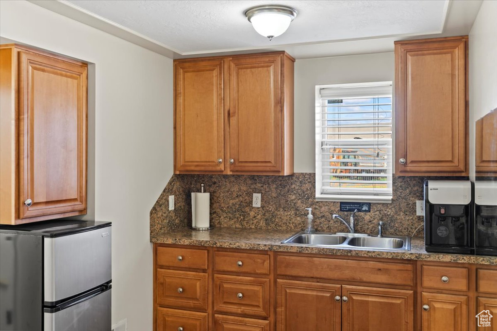Kitchen with a sink, freestanding refrigerator, tasteful backsplash, dark countertops, and brown cabinets