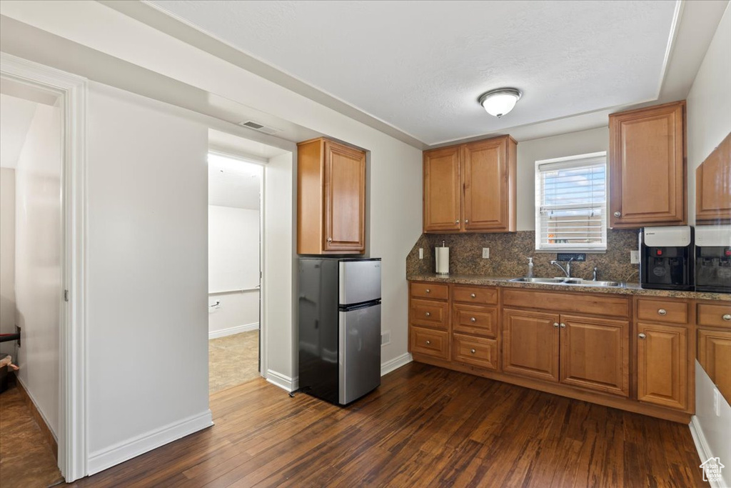 Kitchen featuring freestanding refrigerator, a sink, dark wood finished floors, tasteful backsplash, and brown cabinets