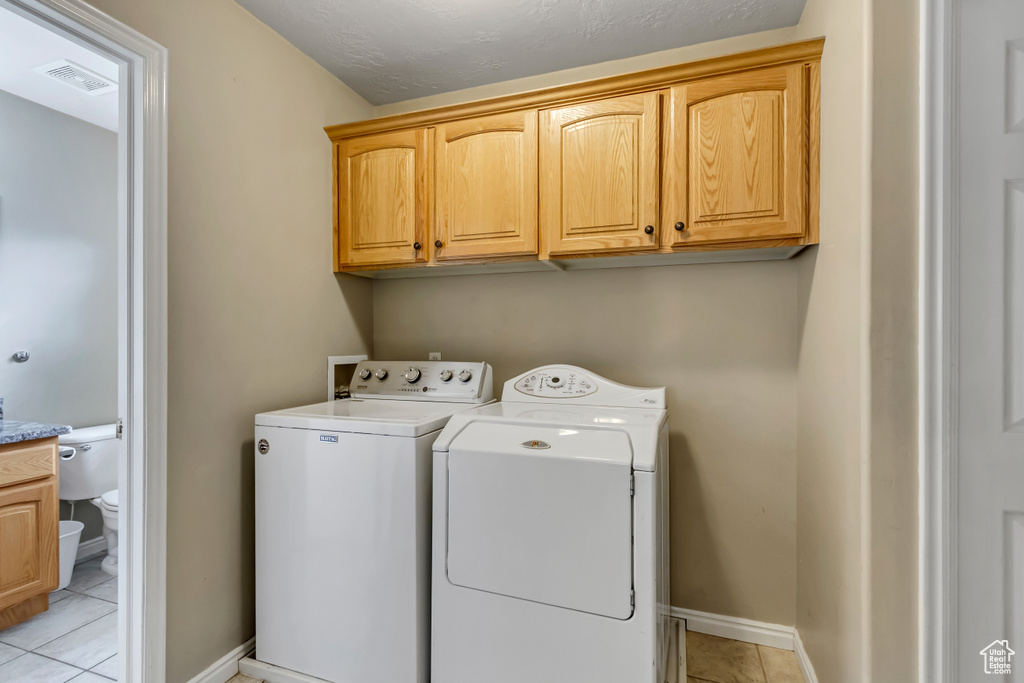 Washroom featuring washing machine and clothes dryer, cabinet space, light tile patterned floors, and baseboards