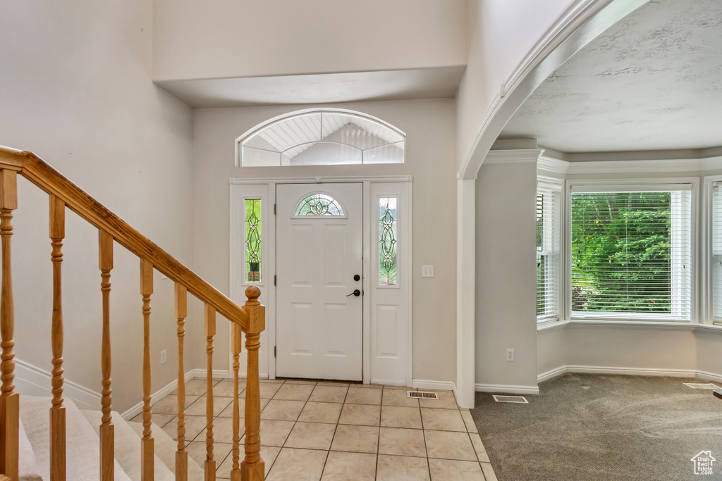 Foyer entrance with arched walkways, baseboards, light tile patterned floors, stairway, and light carpet