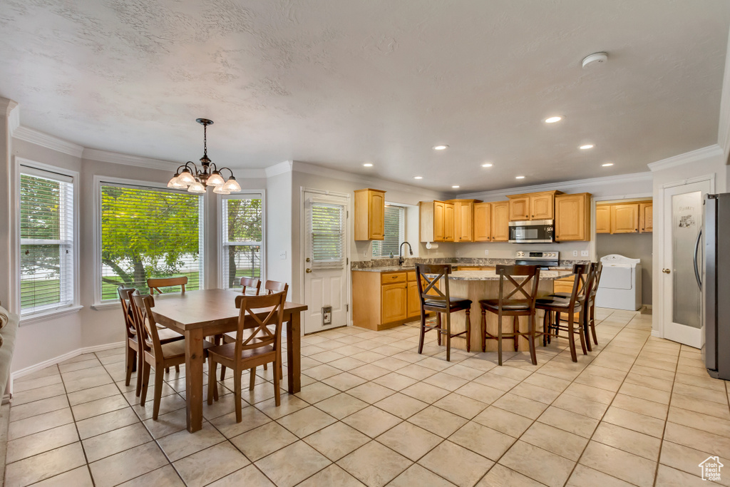 Dining area with washer / clothes dryer, light tile patterned flooring, crown molding, a chandelier, and baseboards