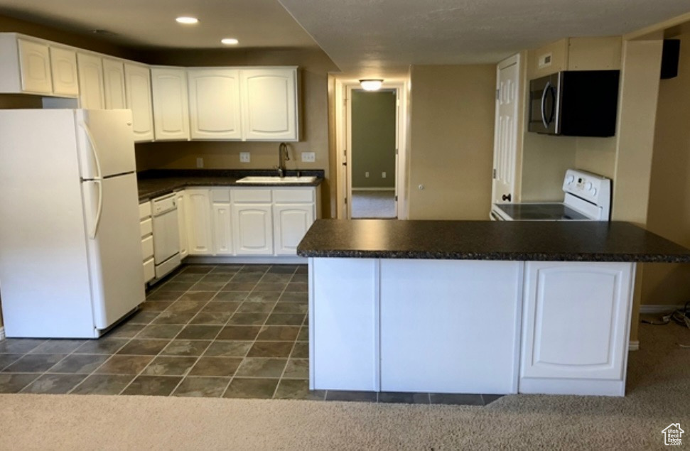 Kitchen with white appliances, a sink, dark countertops, a peninsula, and white cabinets