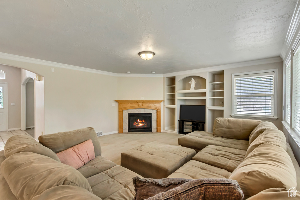 Living area featuring arched walkways, plenty of natural light, a tiled fireplace, crown molding, and a textured ceiling