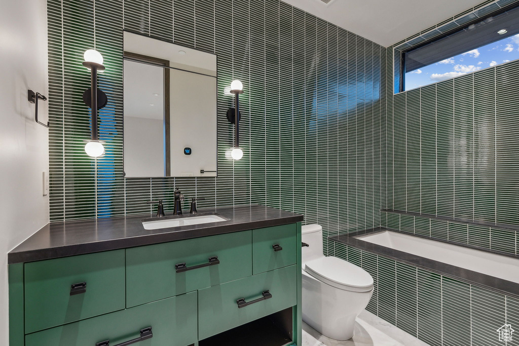 Bathroom featuring tile walls, toilet, a relaxing tiled tub, vanity, and tasteful backsplash