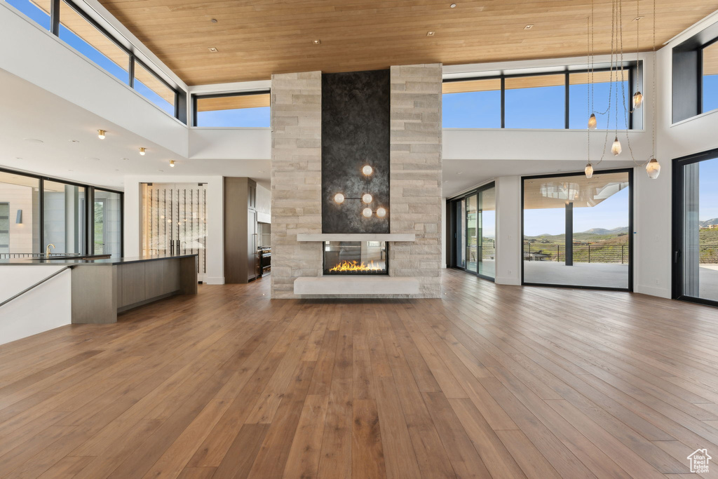 Unfurnished living room with a towering ceiling, a multi sided fireplace, wooden ceiling, wood-type flooring, and healthy amount of natural light
