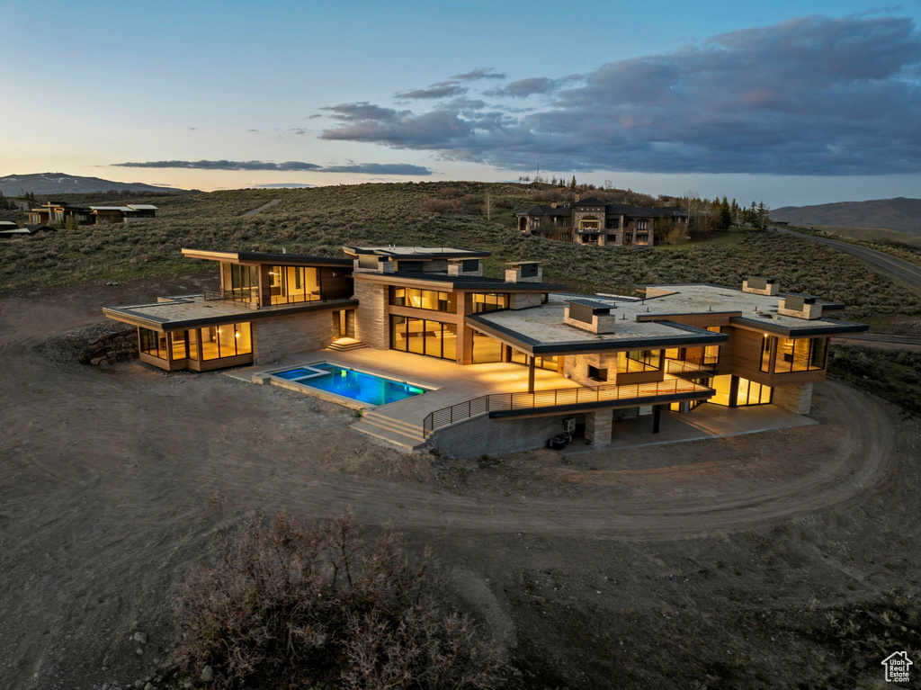 Back of property at dusk with an outdoor pool, a balcony, a mountain view, and dirt driveway