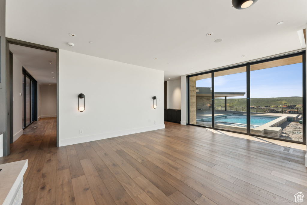 Unfurnished room featuring a wall of windows, hardwood / wood-style flooring, and baseboards