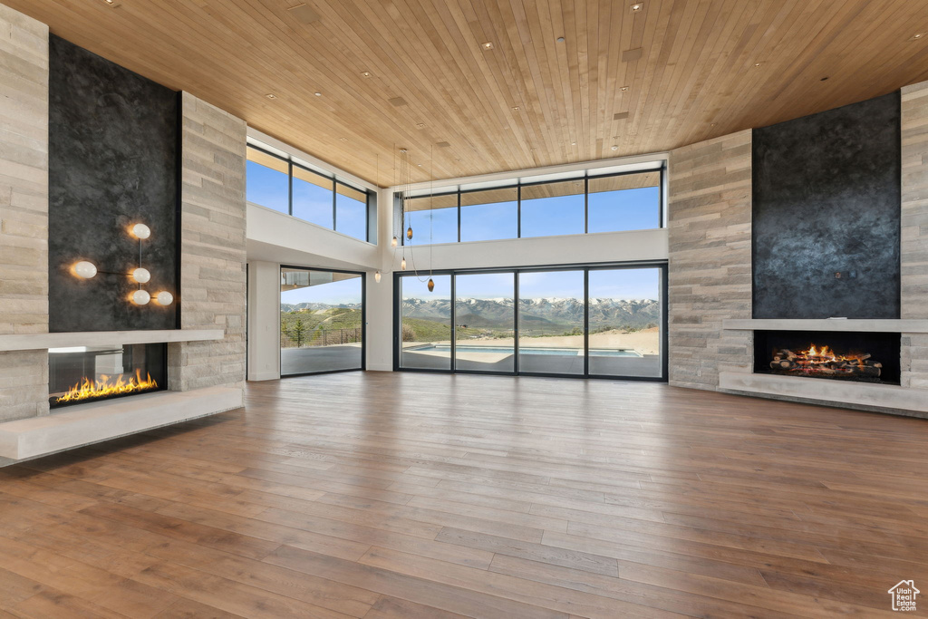 Unfurnished living room with a stone fireplace, a high ceiling, wooden ceiling, plenty of natural light, and hardwood / wood-style flooring
