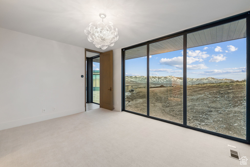 Spare room with expansive windows, a chandelier, a mountain view, and carpet flooring