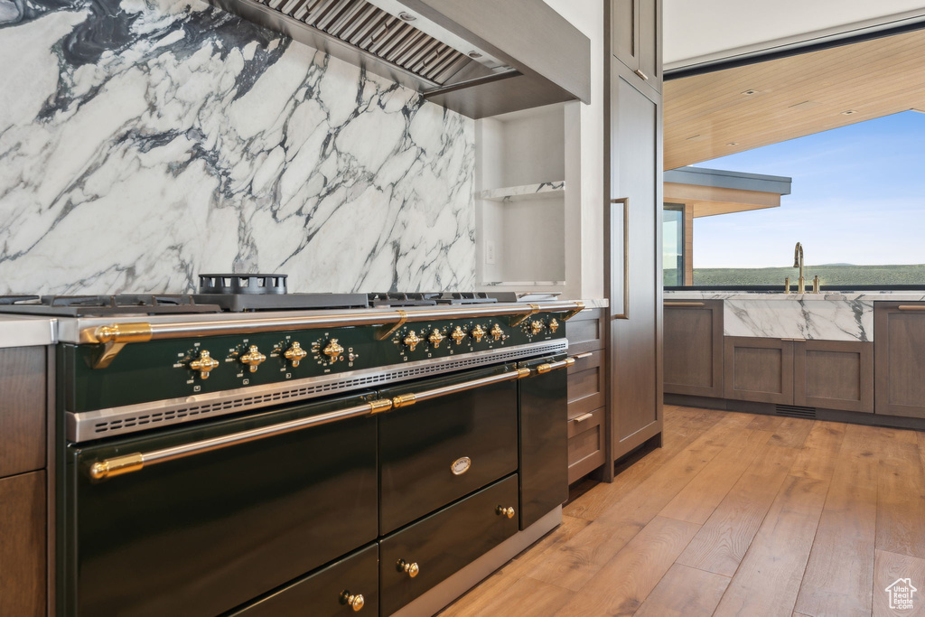 Kitchen view of a sink, range with two ovens, light wood finished floors, and backsplash