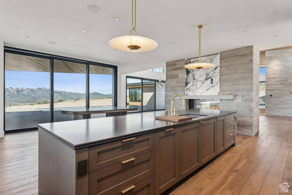 Kitchen featuring dark countertops, a sink, an island with sink, light wood-style floors, and expansive windows