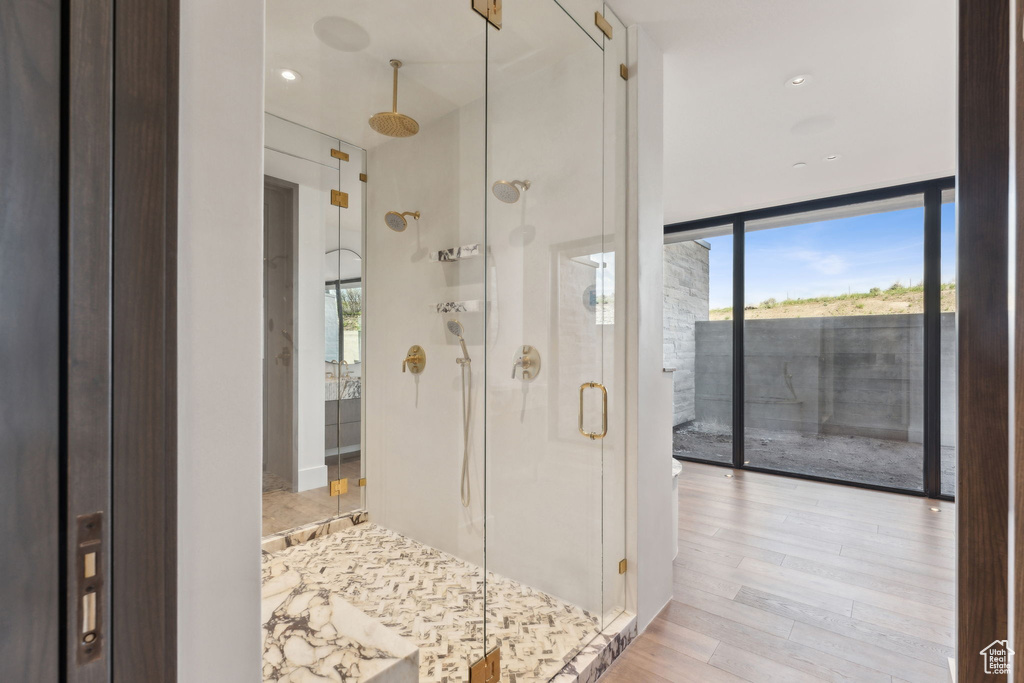 Bathroom featuring healthy amount of natural light, a stall shower, wood finished floors, and a wall of windows