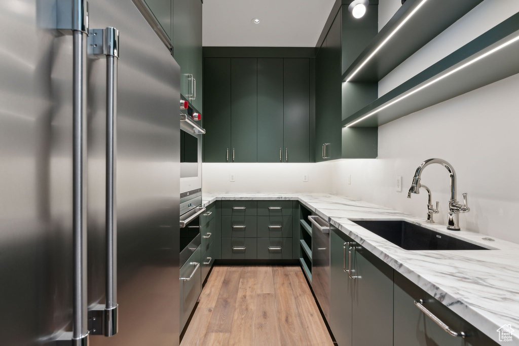 Kitchen featuring stainless steel appliances, a sink, light stone counters, light wood-style flooring, and green cabinetry