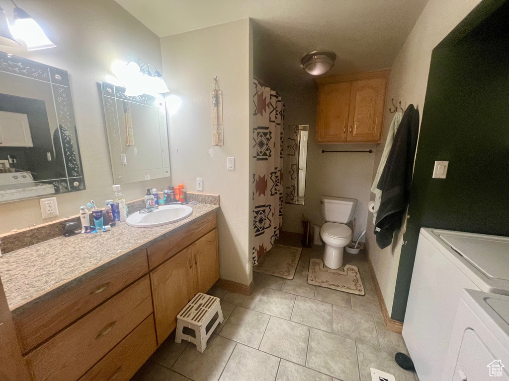 Full bath featuring washing machine and dryer, toilet, tile patterned flooring, vanity, and baseboards