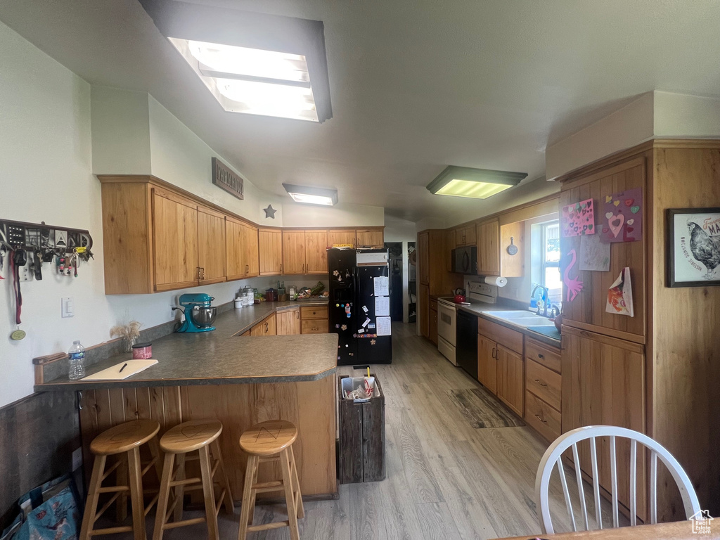 Kitchen with black appliances, a peninsula, a sink, light wood-style flooring, and a breakfast bar area