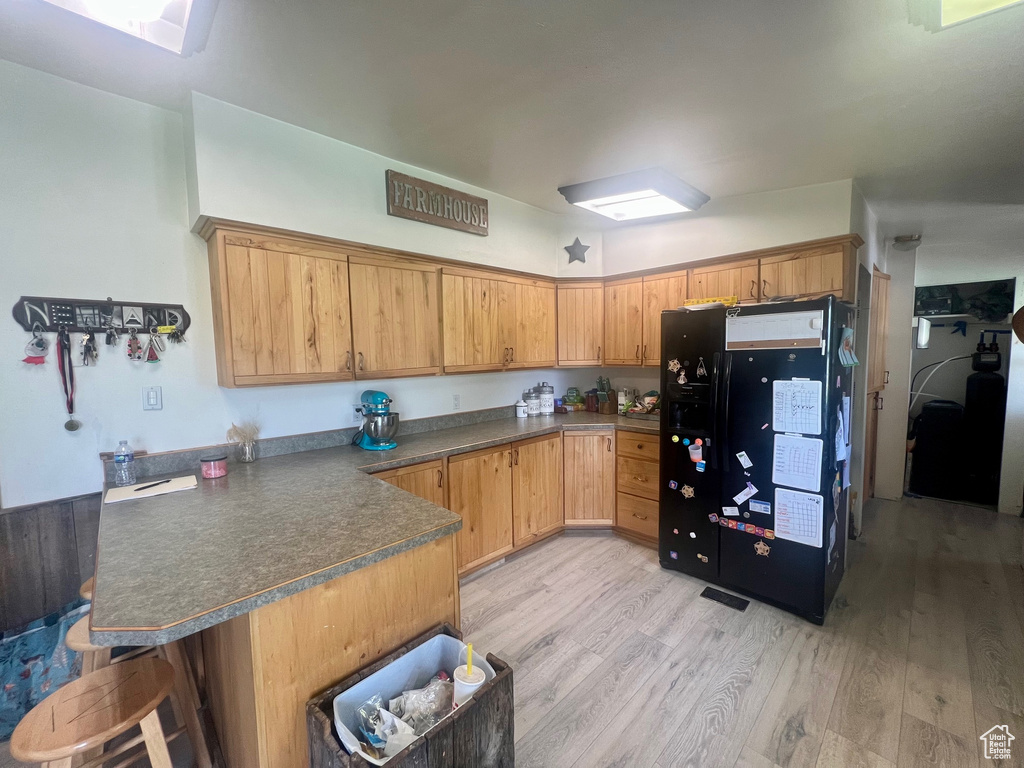 Kitchen with black refrigerator with ice dispenser, a peninsula, light wood-style floors, and dark countertops