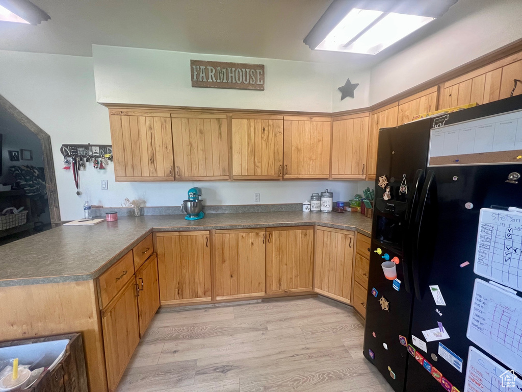 Kitchen featuring black refrigerator with ice dispenser, a peninsula, dark countertops, and light wood-style flooring