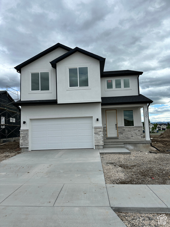 View of front of property featuring stone siding, a garage, driveway, stucco siding, and covered porch