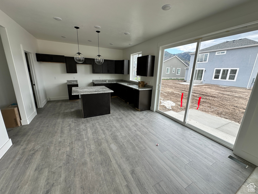 Kitchen with dark cabinetry, wood finished floors, a center island, pendant lighting, and baseboards