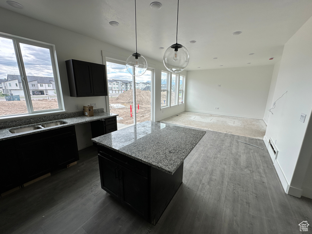 Kitchen with dark cabinetry, a sink, wood finished floors, light stone countertops, and pendant lighting