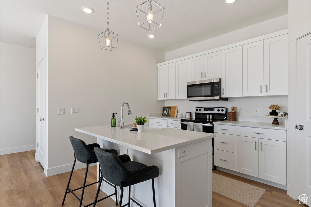 Kitchen featuring appliances with stainless steel finishes, a breakfast bar, hanging light fixtures, light wood-type flooring, and recessed lighting