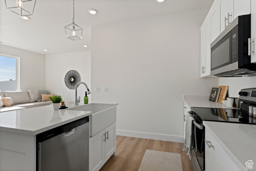 Kitchen with appliances with stainless steel finishes, a sink, light wood finished floors, white cabinetry, and recessed lighting