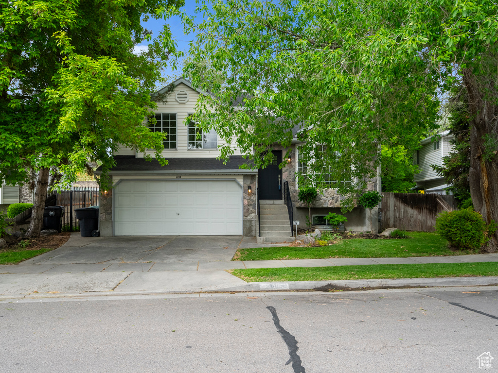 View of property hidden behind natural elements with fence, concrete driveway, a garage, and stone siding