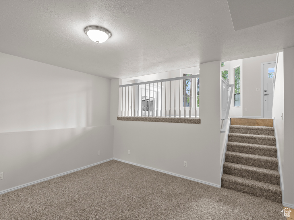 Carpeted empty room featuring a textured ceiling, baseboards, and stairway