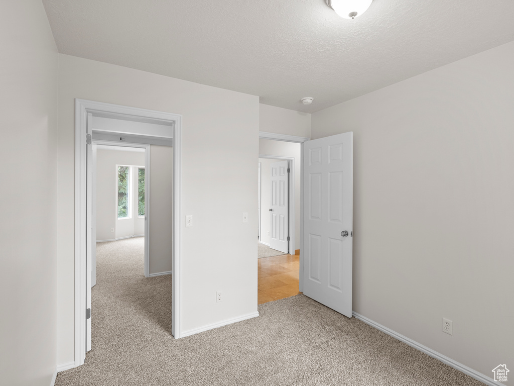 Unfurnished bedroom featuring light carpet, baseboards, and a textured ceiling