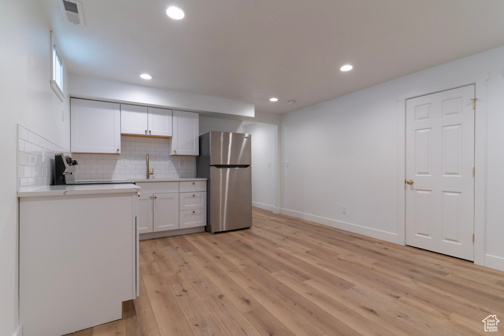 Kitchen featuring freestanding refrigerator, white cabinetry, light countertops, light wood-type flooring, and backsplash