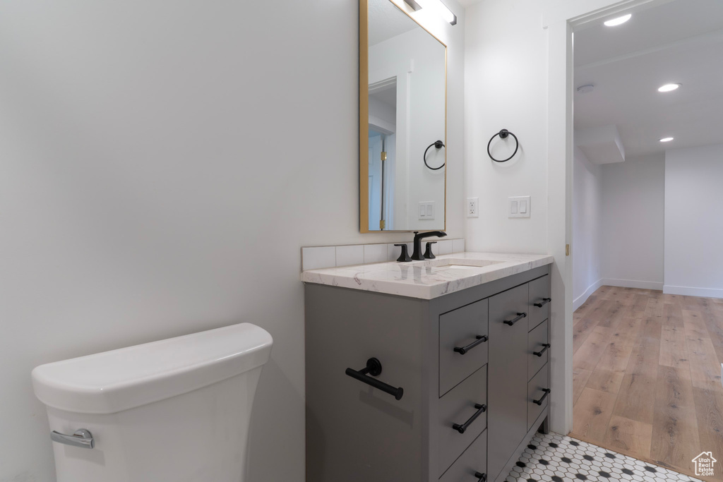 Half bathroom with recessed lighting, vanity, toilet, and wood finished floors