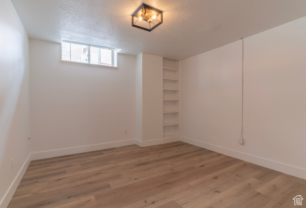 Basement with light wood-style floors, baseboards, and a textured ceiling
