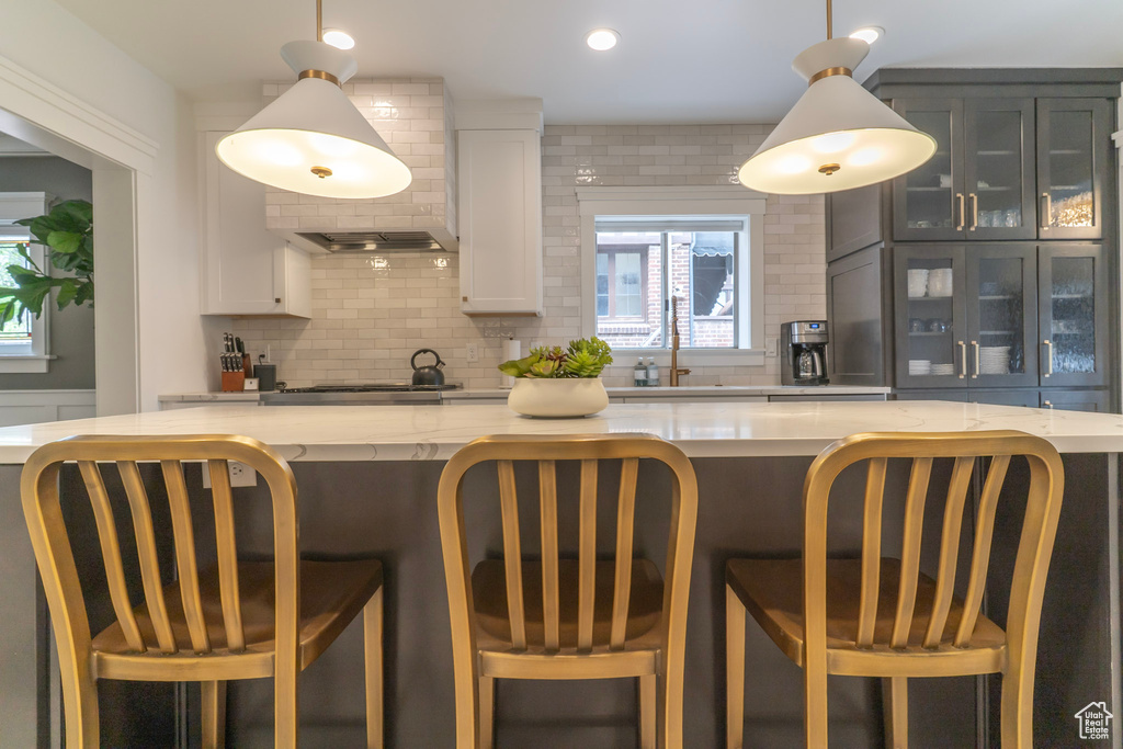 Kitchen with backsplash, white cabinets, glass insert cabinets, light stone countertops, and recessed lighting