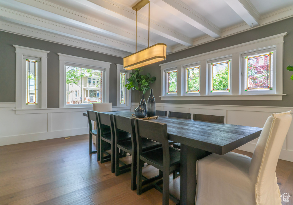 Dining space with beamed ceiling, wood finished floors, wainscoting, and a decorative wall