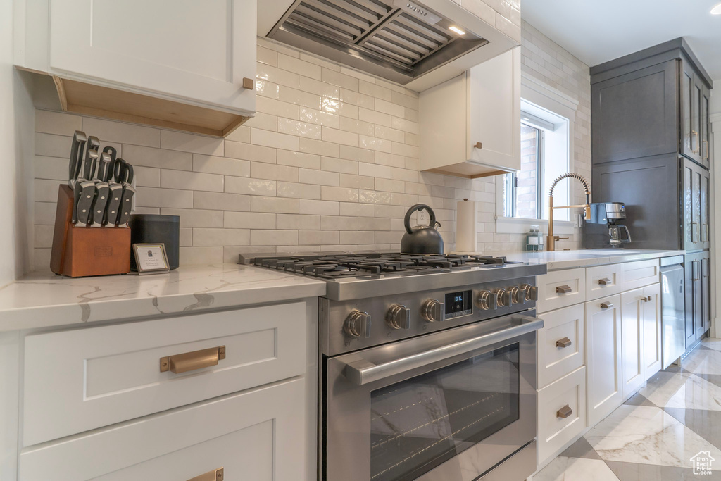 Kitchen with appliances with stainless steel finishes, custom range hood, a sink, light stone countertops, and decorative backsplash