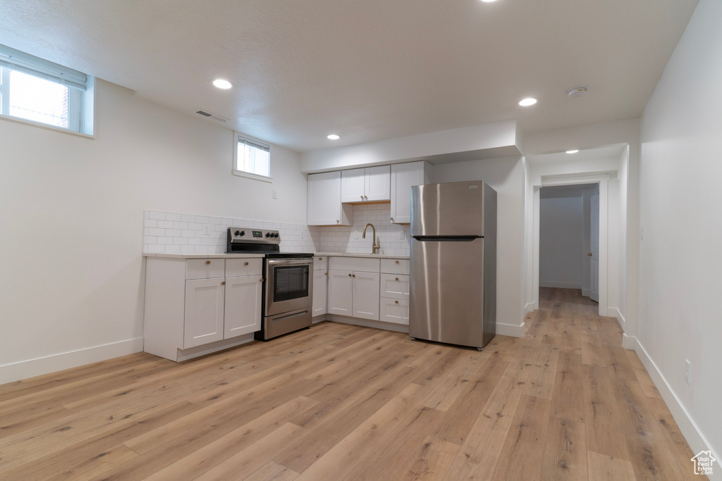 Kitchen featuring stainless steel appliances, a sink, white cabinets, decorative backsplash, and light countertops