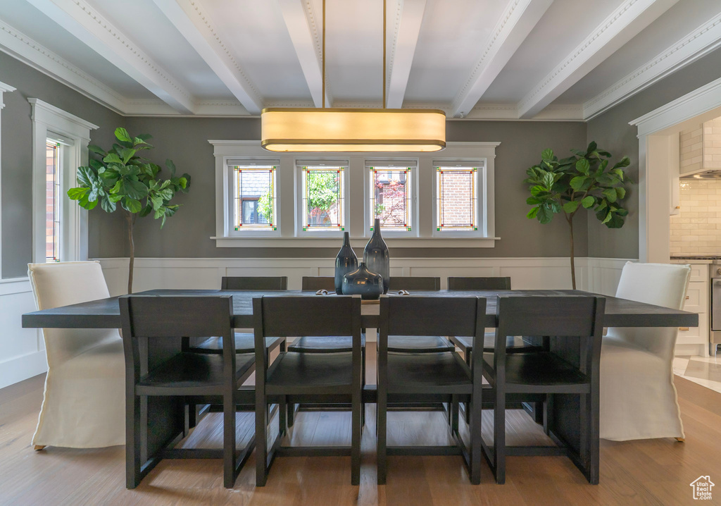 Dining space with plenty of natural light, beamed ceiling, wood finished floors, wainscoting, and crown molding
