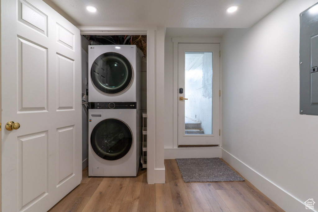 Laundry room with stacked washer / drying machine, light wood-style floors, recessed lighting, electric panel, and baseboards