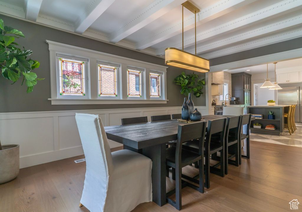 Dining space with beam ceiling, wood-type flooring, a decorative wall, and a wainscoted wall