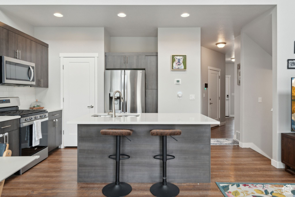 Kitchen with stainless steel appliances, a sink, a breakfast bar, dark wood-type flooring, and an island with sink