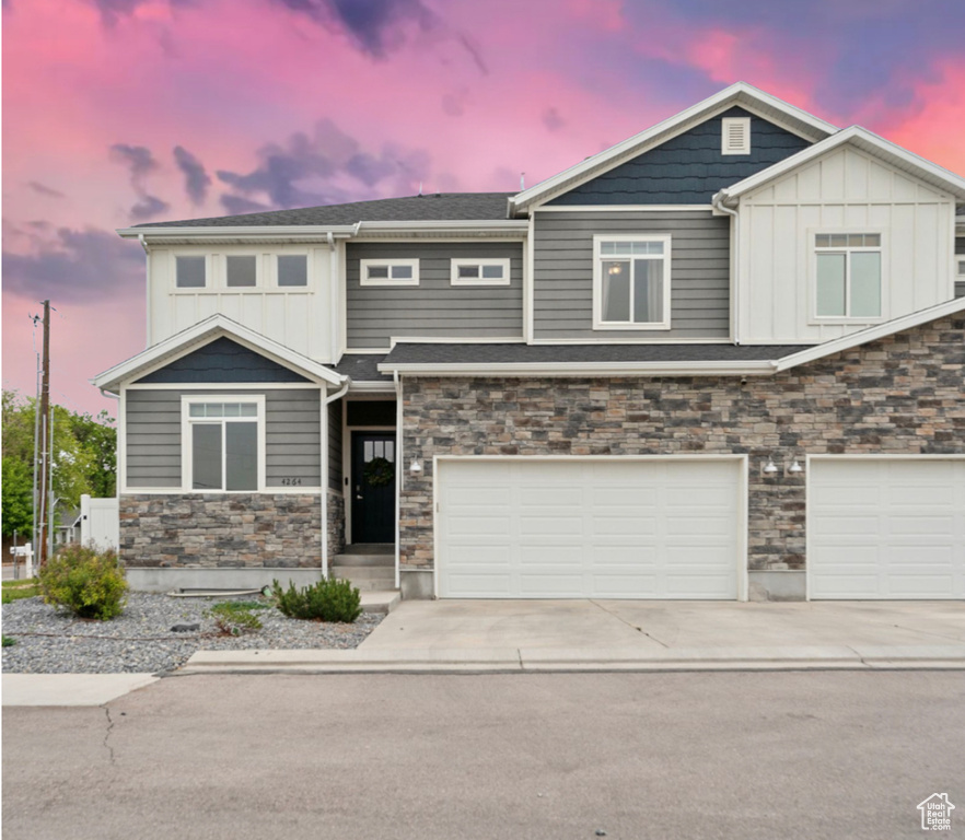 View of front facade featuring stone siding, an attached garage, concrete driveway, and board and batten siding