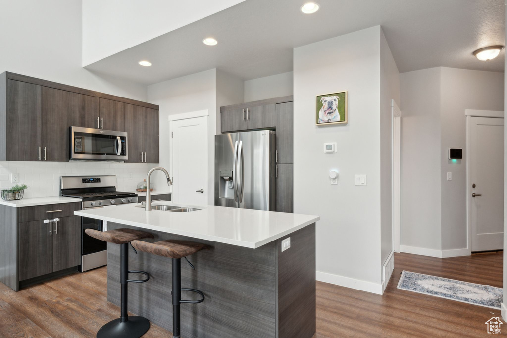 Kitchen with stainless steel appliances, a sink, a kitchen breakfast bar, light countertops, and wood finished floors
